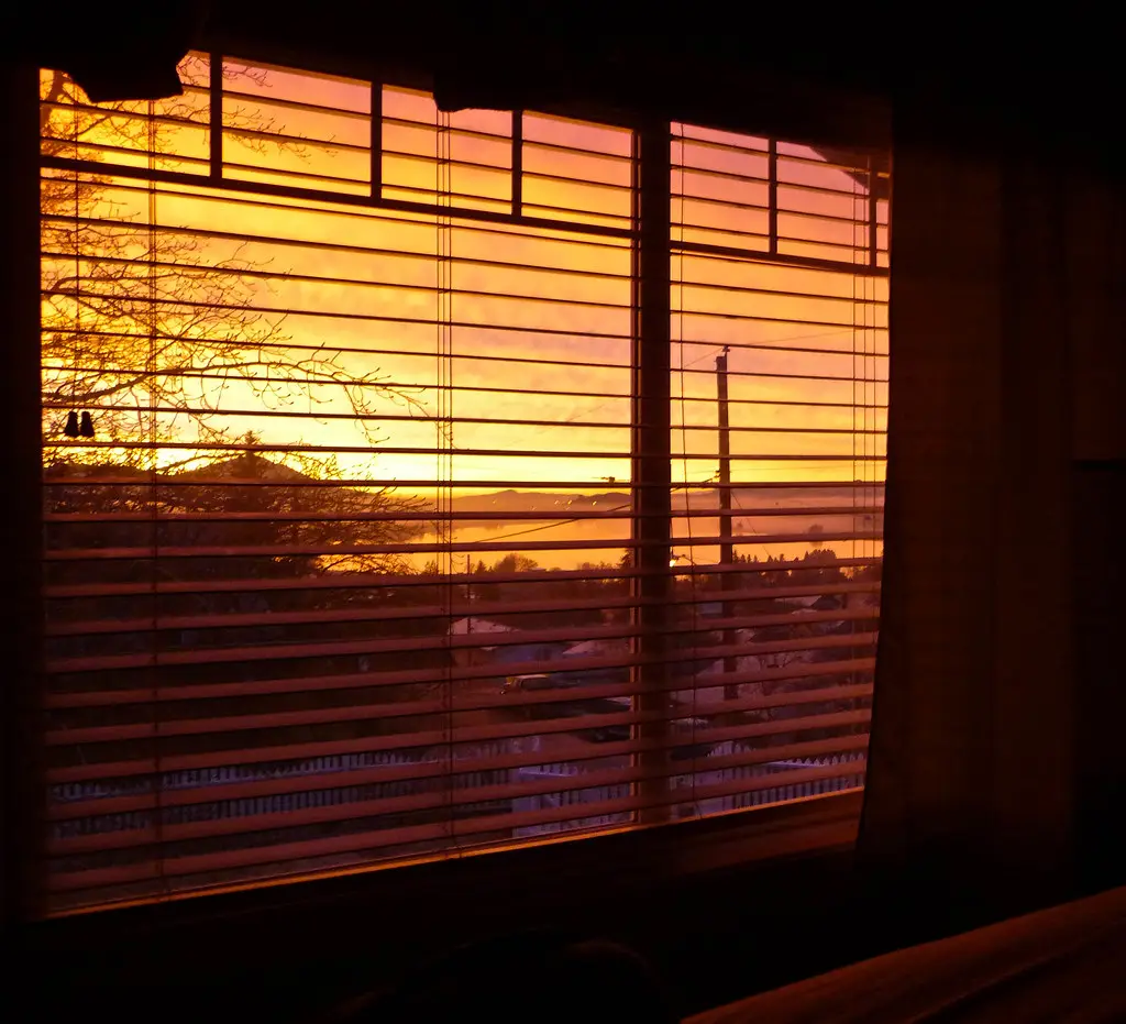 Sonnenaufgang scheint durch ein Schlafzimmerfenster mit heruntergelassener Jalousie